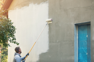 a person painting a home’s exterior with a roller